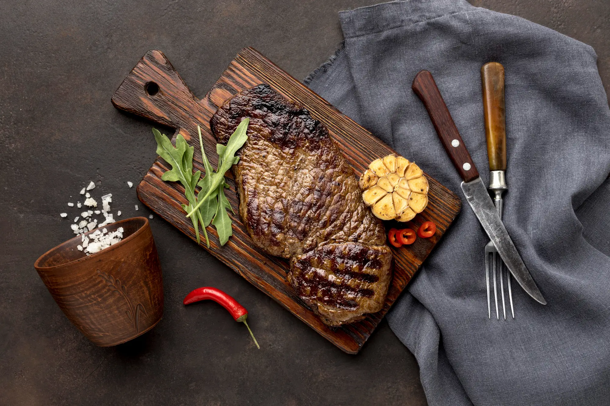 Steak resting on a board beside a carving fork and knife